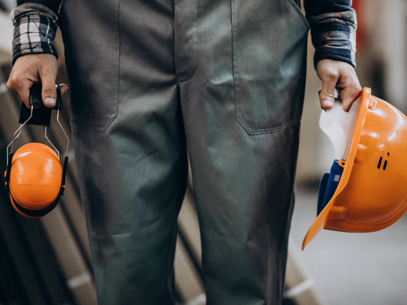 Sicherheitsbeauftragter Kompakt - Handwerk und Industrie bei HSE-CAMPUS in Münster - Mann in Schutzkleidung hält orangenen Helm in der einen und orangene Ohrenschützer in der anderen Hand