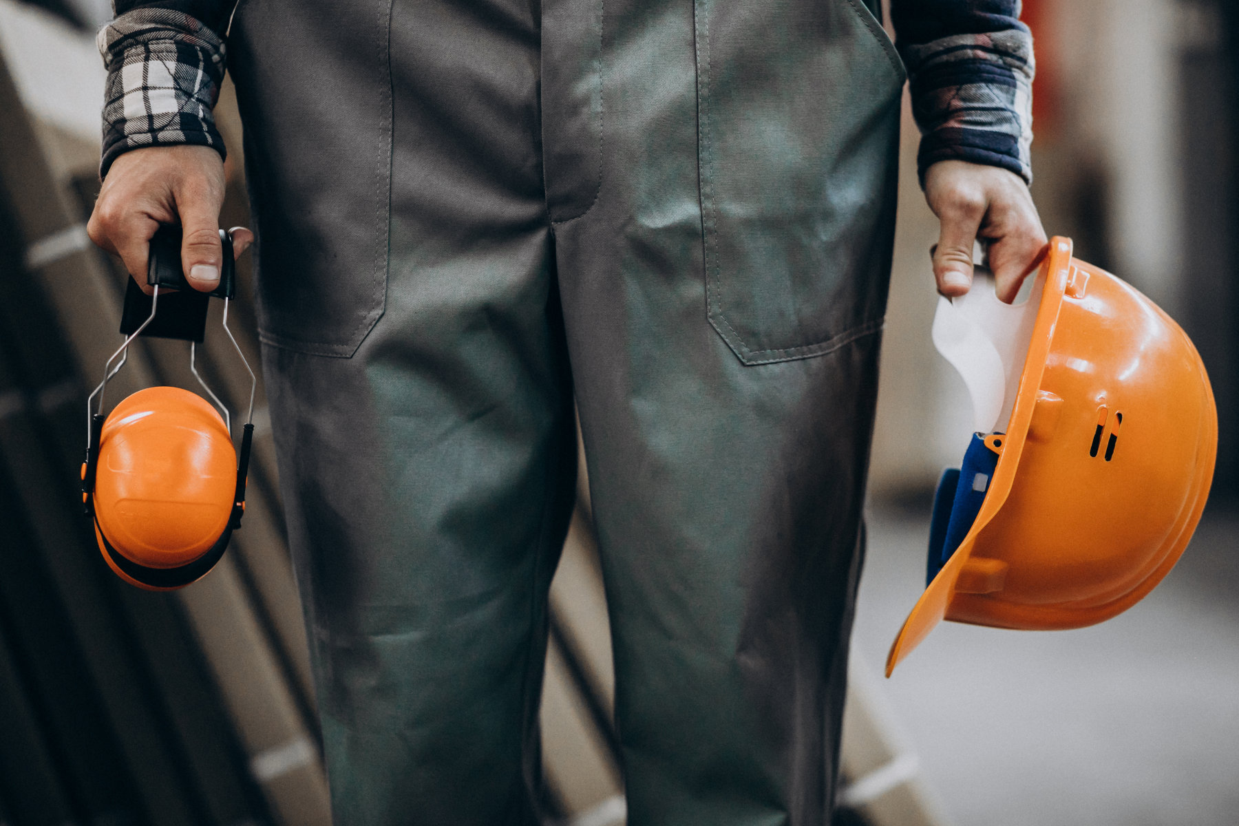 Sicherheitsbeauftragter Kompakt - Handwerk und Industrie bei HSE-CAMPUS in Münster - Mann in Schutzkleidung hält orangenen Helm in der einen und orangene Ohrenschützer in der anderen Hand
